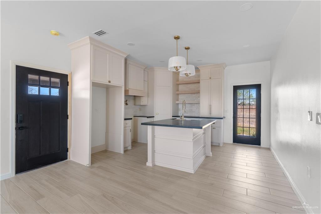 311 Other Road Rio Grande City, TX 78582 - Photo 6 of 16 Kitchen with dark countertops, a center island with sink, light wood-style floors, decorative light fixtures, and tasteful backsplash