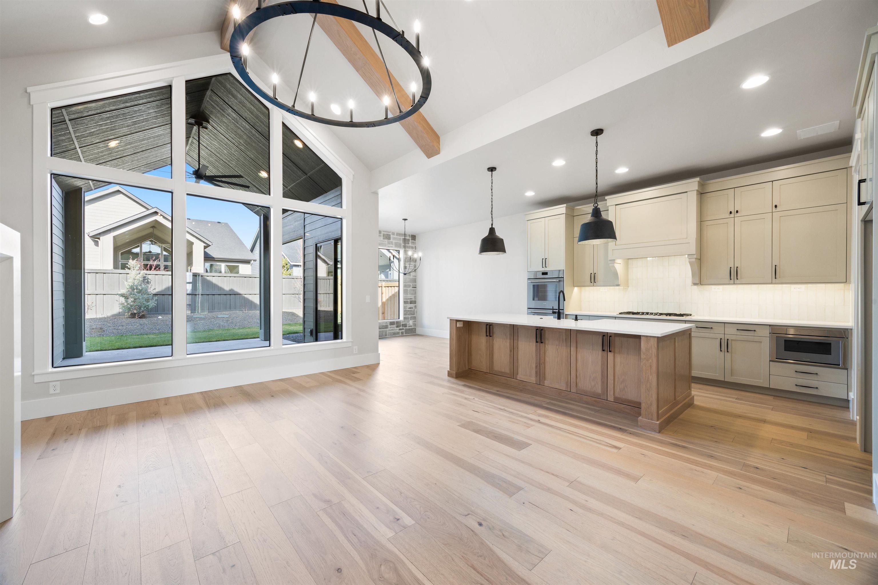 1048 East Escalation Street Meridian, ID 83642 - Photo 11 of 44 Kitchen featuring a chandelier, two tone color scheme, an island with sink, backsplash, and light wood finished floors
