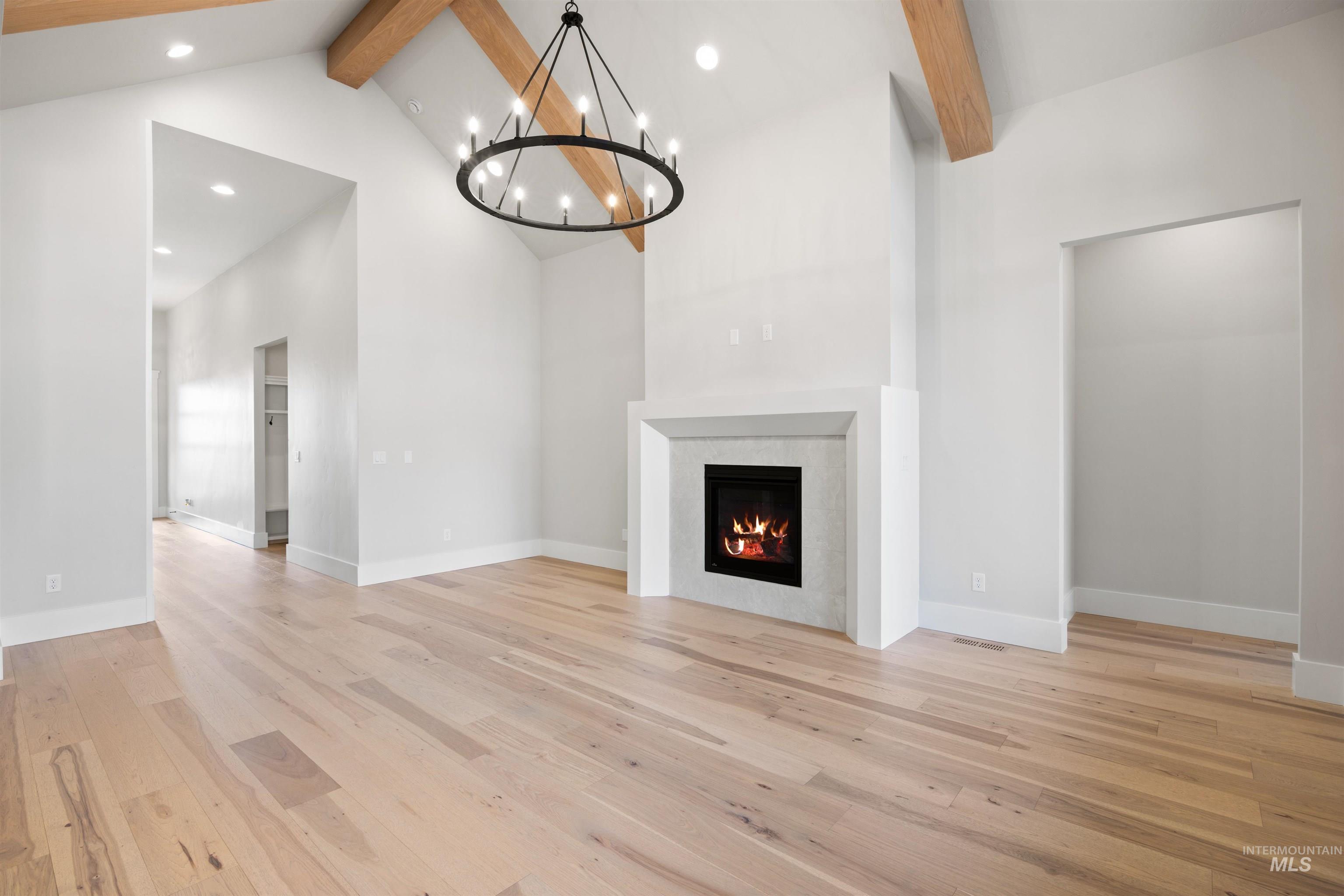 1048 East Escalation Street Meridian, ID 83642 - Photo 13 of 44 Unfurnished living room featuring a chandelier, light wood finished floors, and a warm lit fireplace