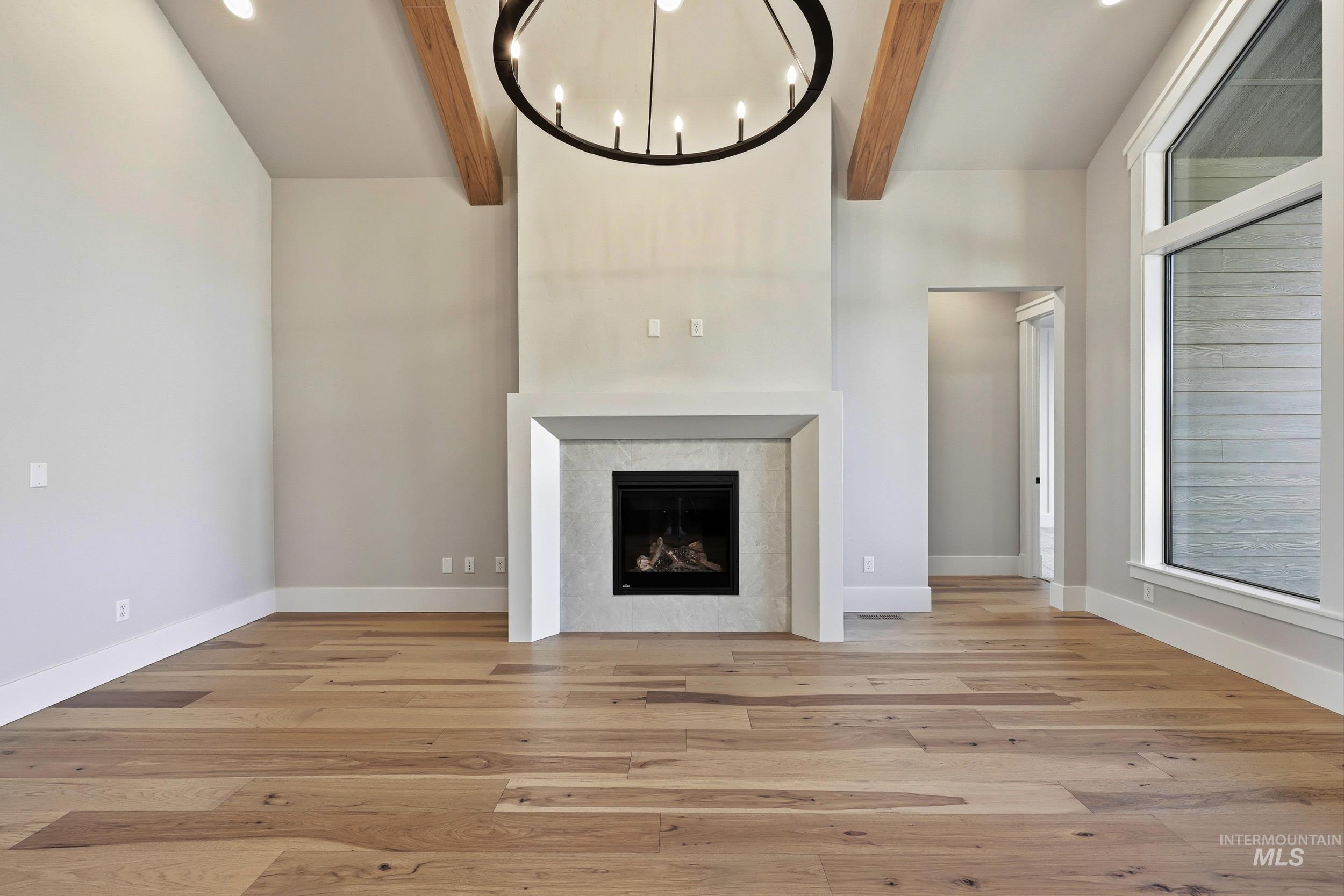 1048 East Escalation Street Meridian, ID 83642 - Photo 16 of 44 Unfurnished living room with a tile fireplace, light wood-style floors, recessed lighting, beam ceiling, and a chandelier