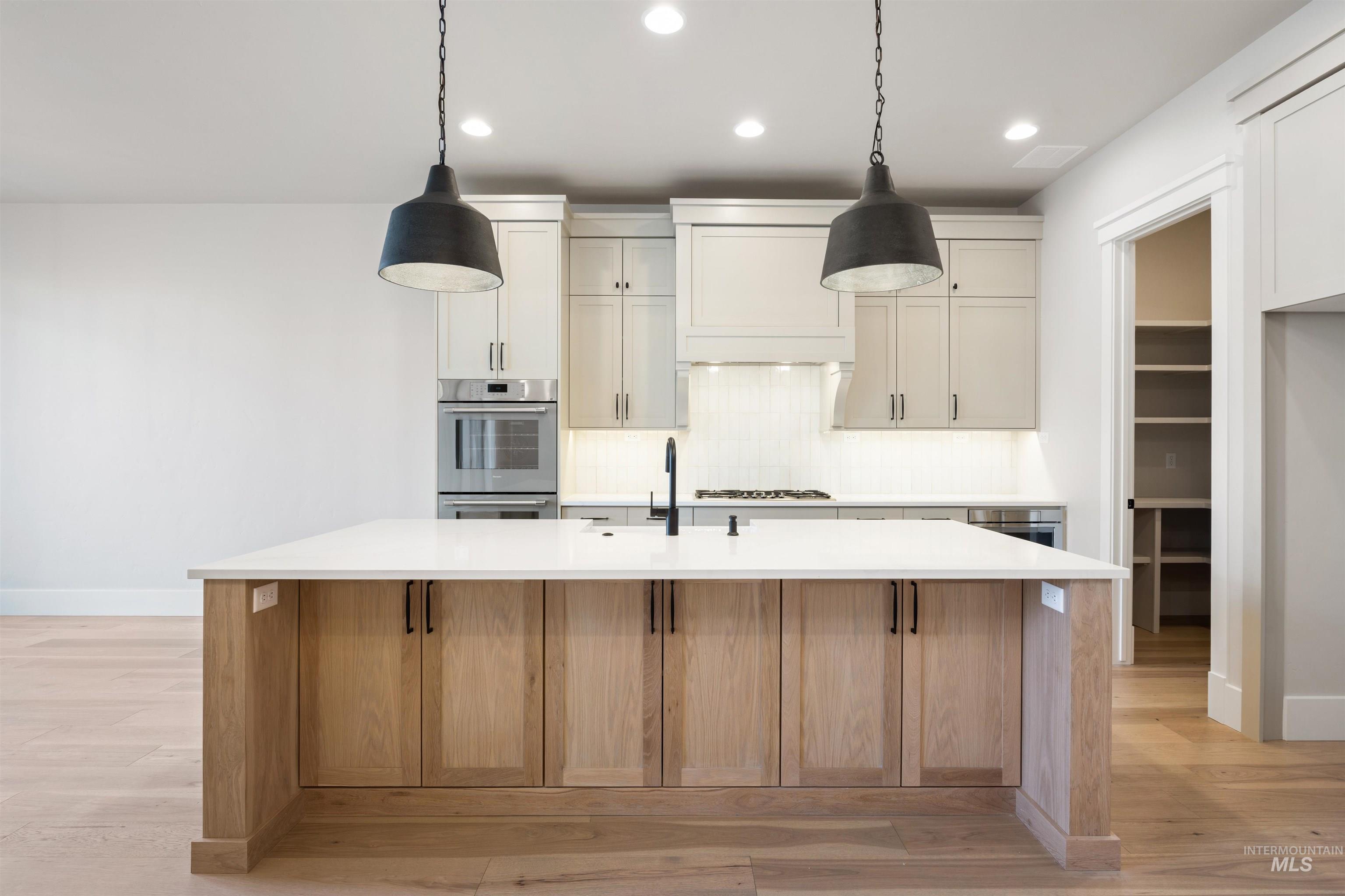 1048 East Escalation Street Meridian, ID 83642 - Photo 20 of 44 Kitchen featuring light wood-type flooring, decorative light fixtures, an island with sink, backsplash, and two tone cabinets