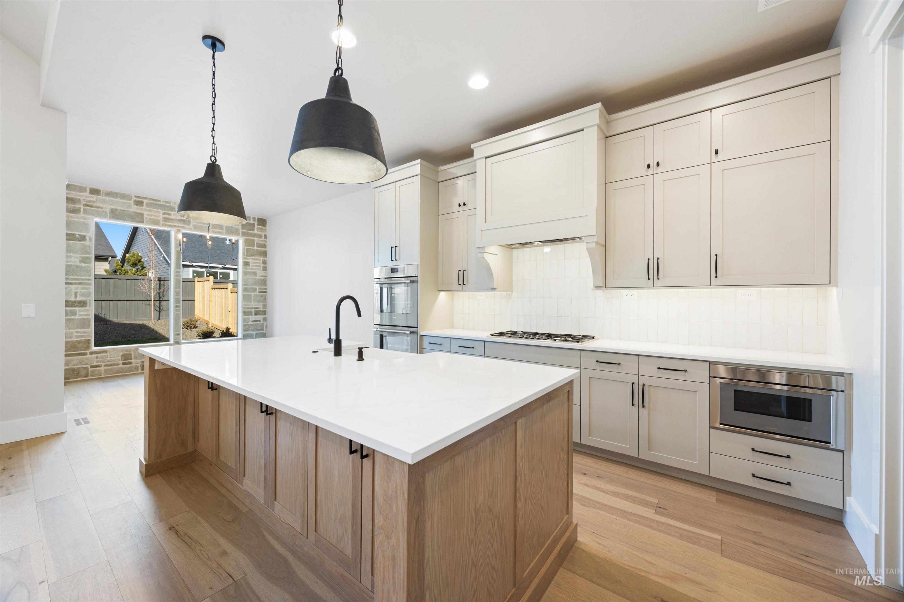 1048 East Escalation Street Meridian, ID 83642 - Photo 21 of 44 Kitchen featuring decorative light fixtures, dual tone cabinetry, an island with sink, light wood-type flooring, and backsplash