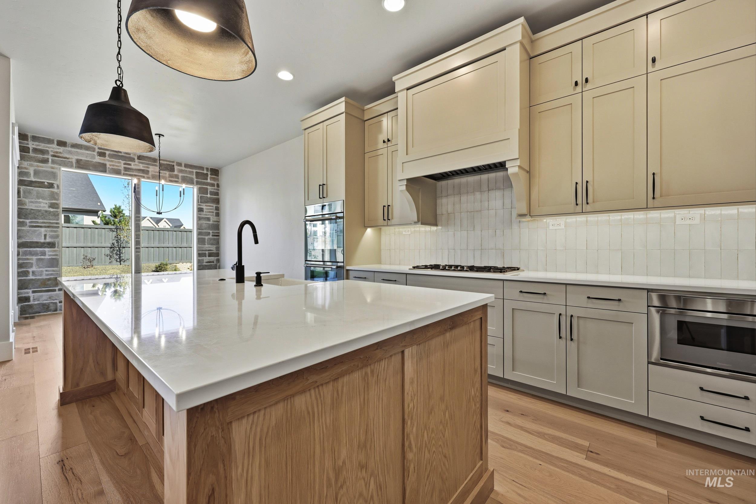 1048 East Escalation Street Meridian, ID 83642 - Photo 6 of 44 Kitchen with decorative light fixtures, a kitchen island with sink, light stone counters, stainless steel double oven, and brown cabinets