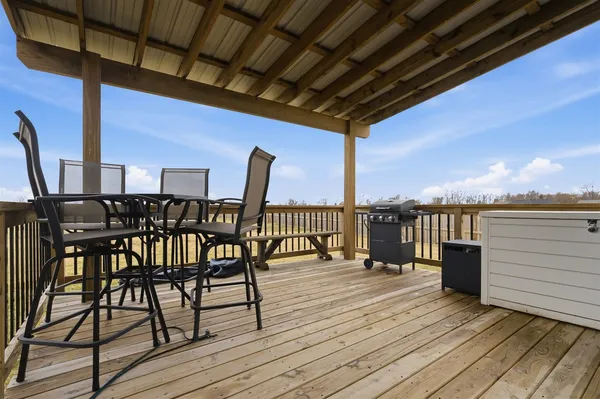 a view of a roof deck with table and chairs a barbeque with wooden floor and fence