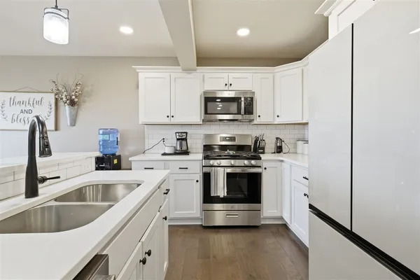a kitchen with stainless steel appliances granite countertop a sink a stove and a refrigerator with wooden floors