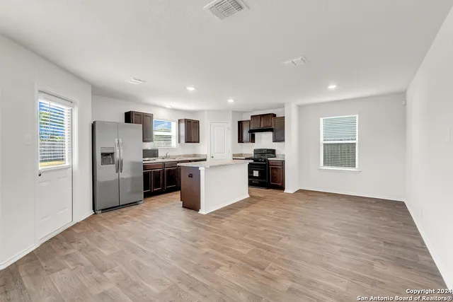 a large white kitchen with stainless steel appliances kitchen island a stove a refrigerator a sink dishwasher and a fireplace with wooden floor