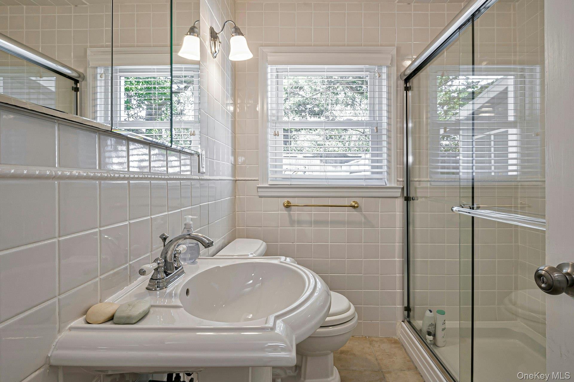 39 Sloop Walk Ocean Beach, NY 11770 - Photo 32 of 46 Bathroom featuring a pedestal sink, white tile walls, a sliding glass shower enclosure, and two windows with blinds