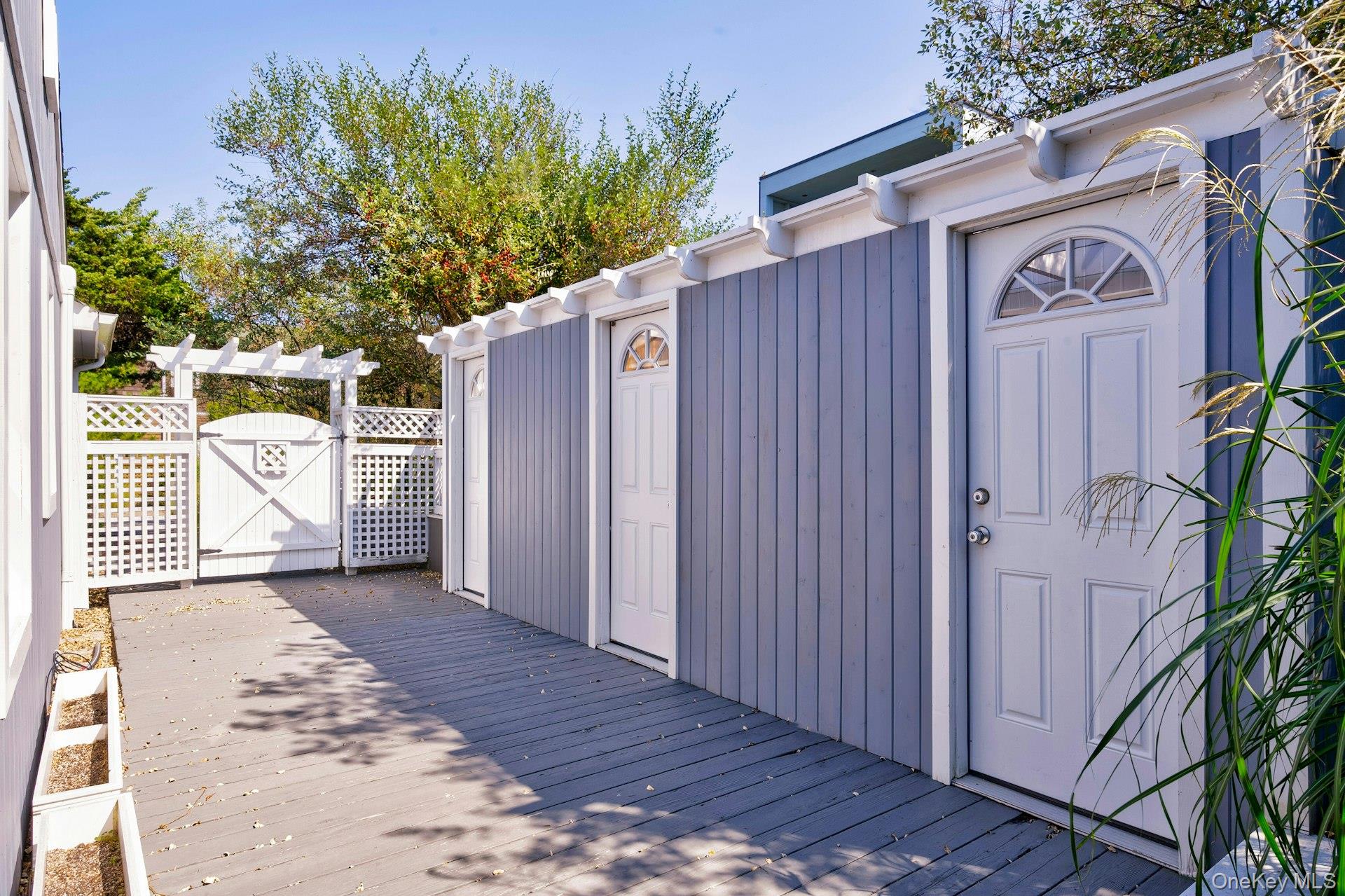 39 Sloop Walk Ocean Beach, NY 11770 - Photo 7 of 46 Exterior space featuring gray wood-finish decking, vertical siding in a muted blue hue, and multiple white paneled doors with arched transom windows
