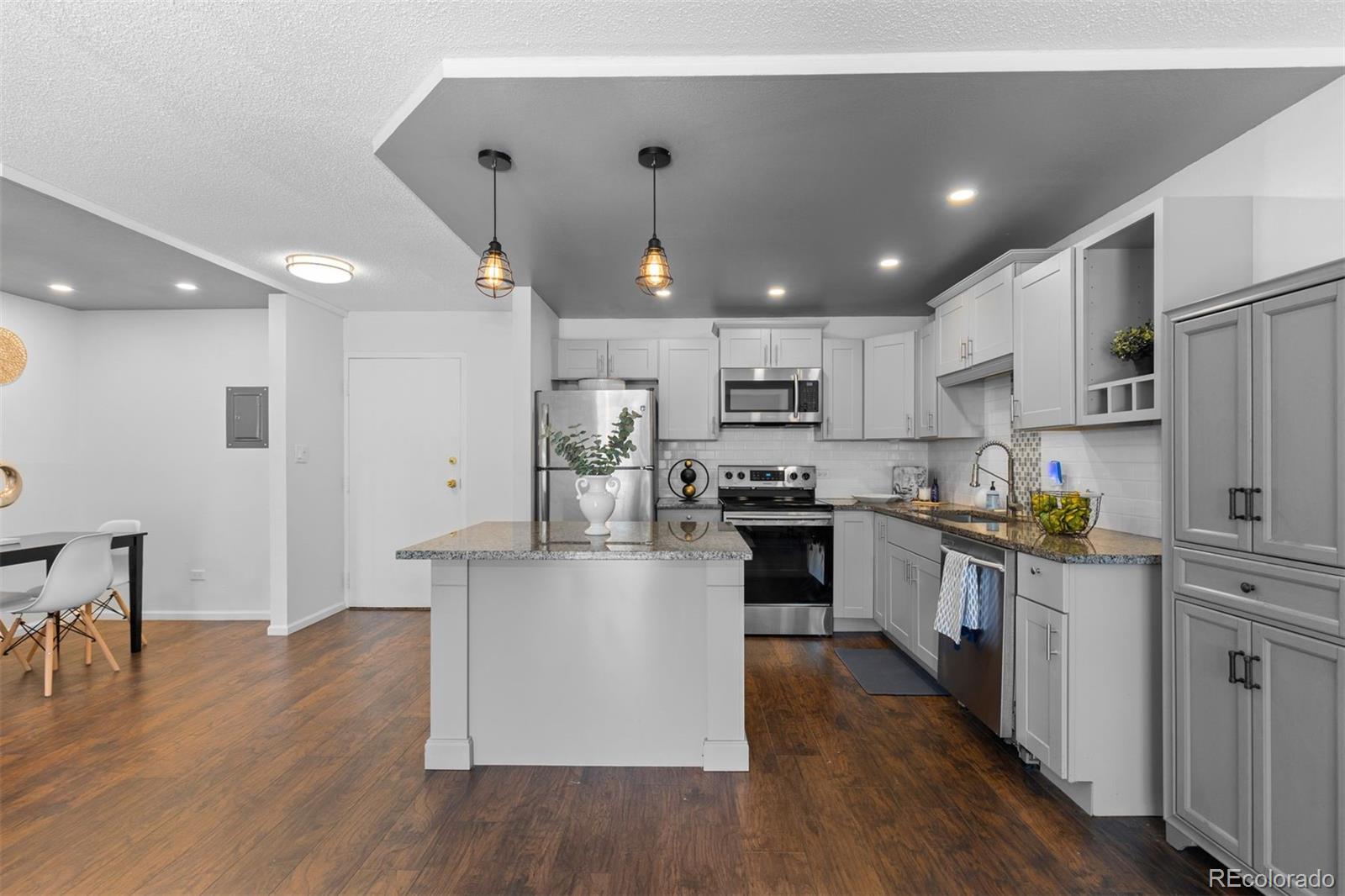 610 South Clinton Street, Unit 10A Denver, CO 80247 - Photo 9 of 40 a kitchen with kitchen island a white counter top space a refrigerator cabinets and a wooden floor
