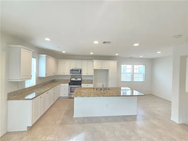 a large kitchen with kitchen island a large counter top and stainless steel appliances