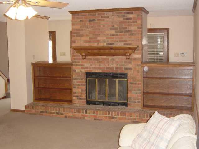 Prefabricated wood fireplace with built in bookcases in carpeted great room.  Ceiling fan in this room.